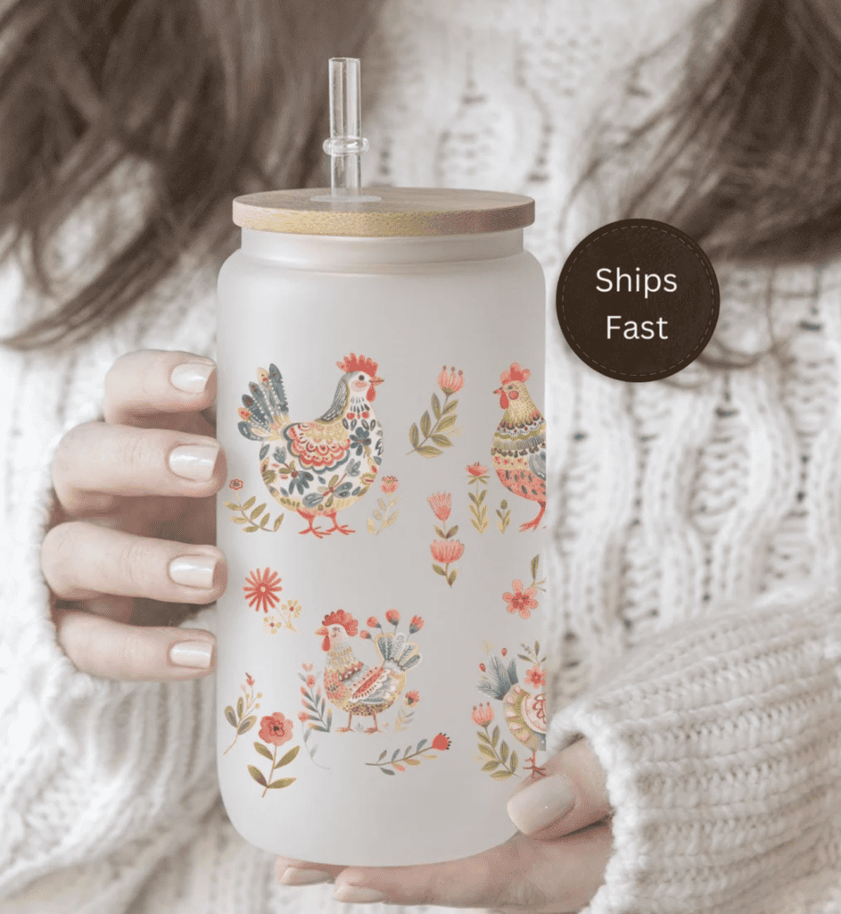 a woman holding a glass tumbler with flower chickens on the front and a brown lid
